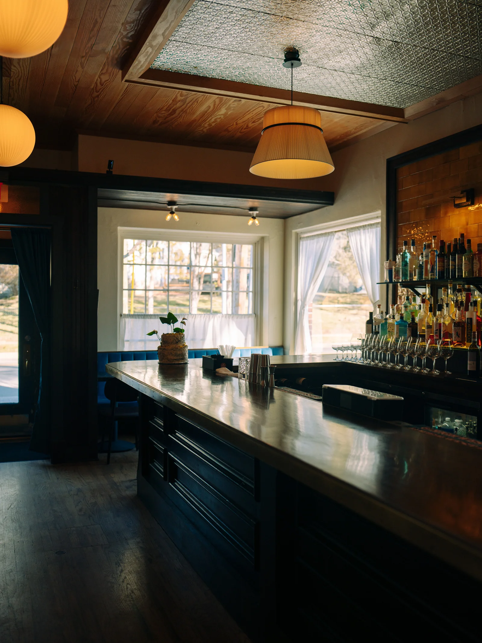 A sunlit bar with warm pendant lamps, a tin ceiling, and bottles along the counter